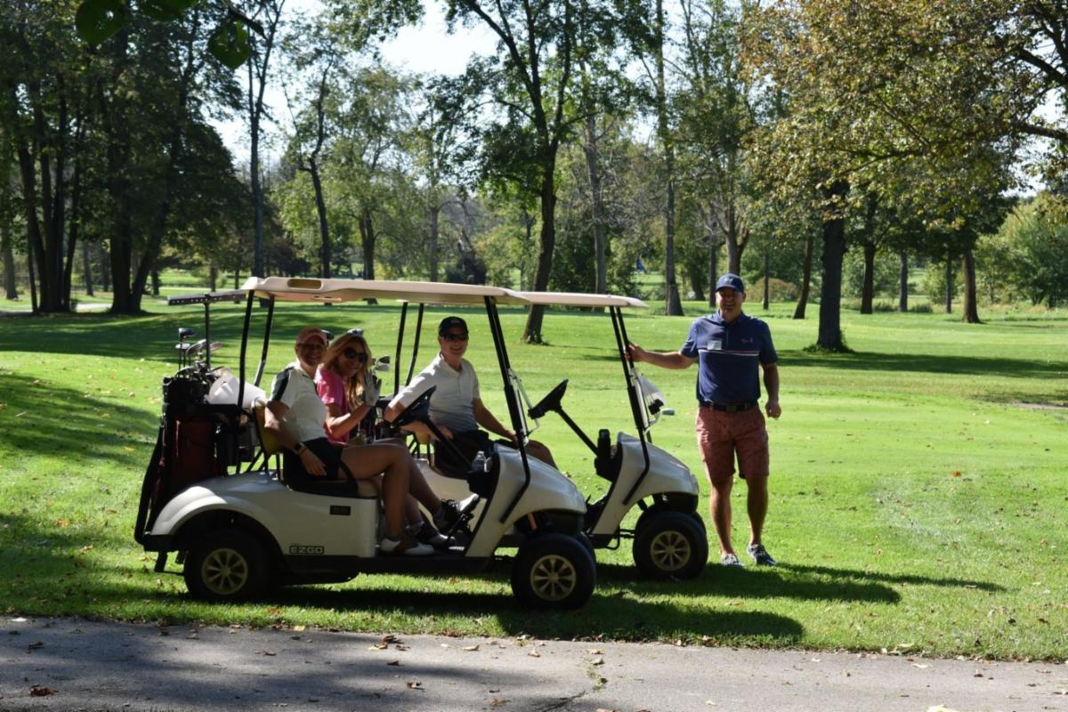 Golfers and a golf cart; the golfers are waving and smiling
